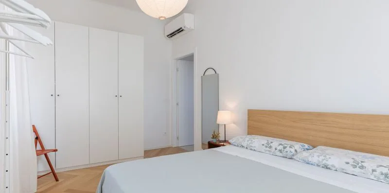 A bright bedroom with a large bed, white wardrobes, and a wooden headboard.