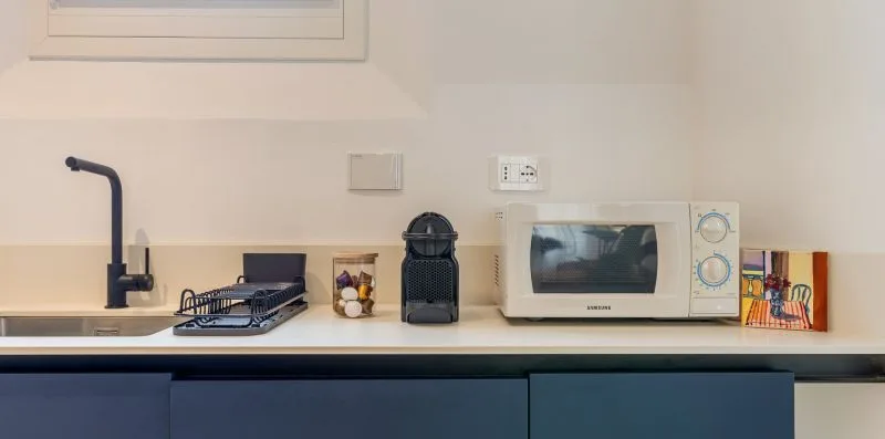 A kitchen counter with a sink, faucet, microwave, and small appliances.