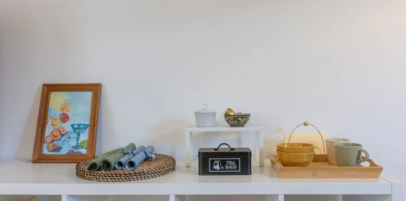 A display shelf holds framed artwork, rolled textiles, tea tins, and cups.