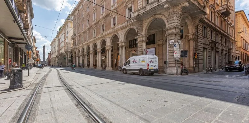 A city street with tram tracks runs past buildings with arched arcades.