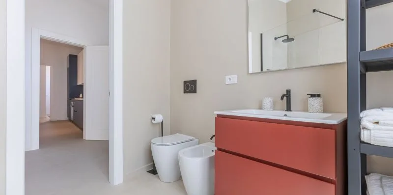 A bathroom with a red vanity, sink, and toilet beside an open doorway.