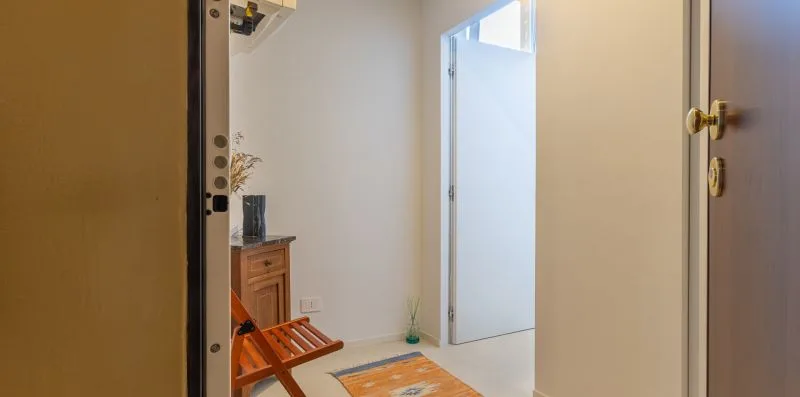 A bright room entryway with an open door and a wooden luggage rack.