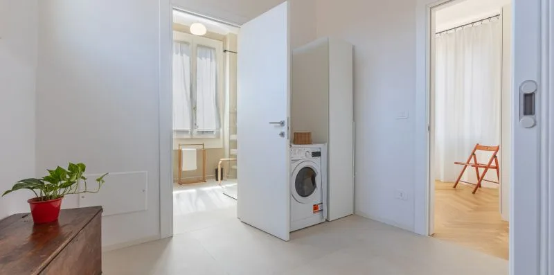 A bright interior hallway with open doorways and a washing machine.
