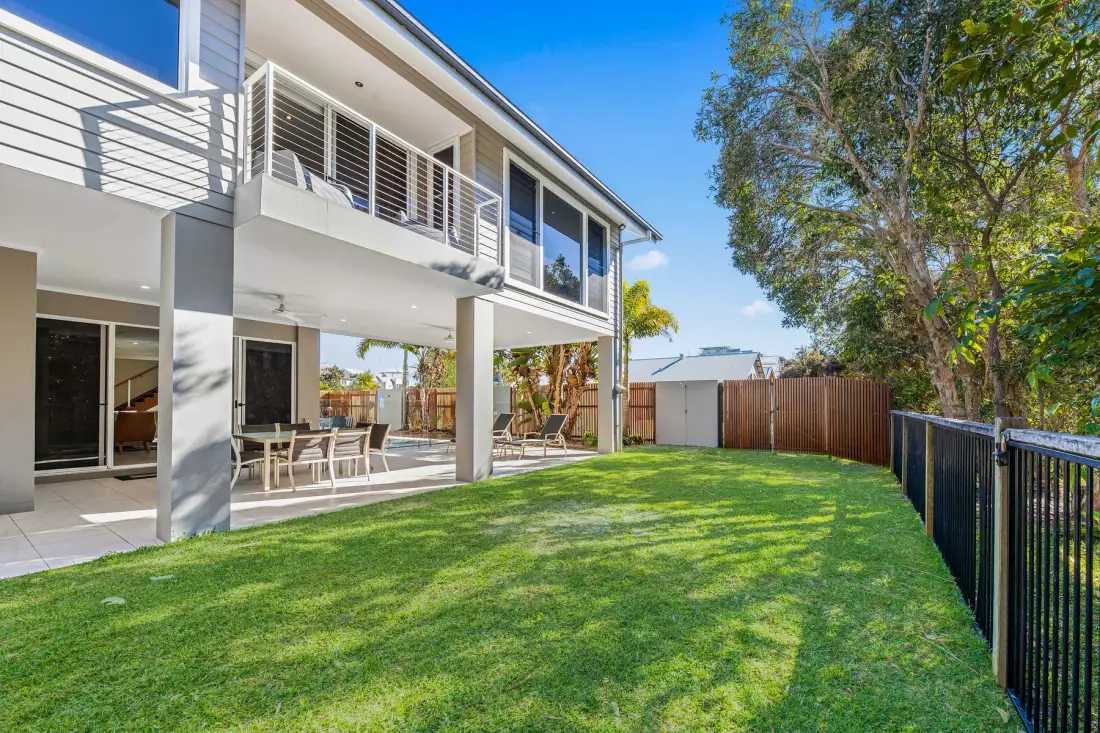 A two-story house overlooks a green lawn with a covered patio.