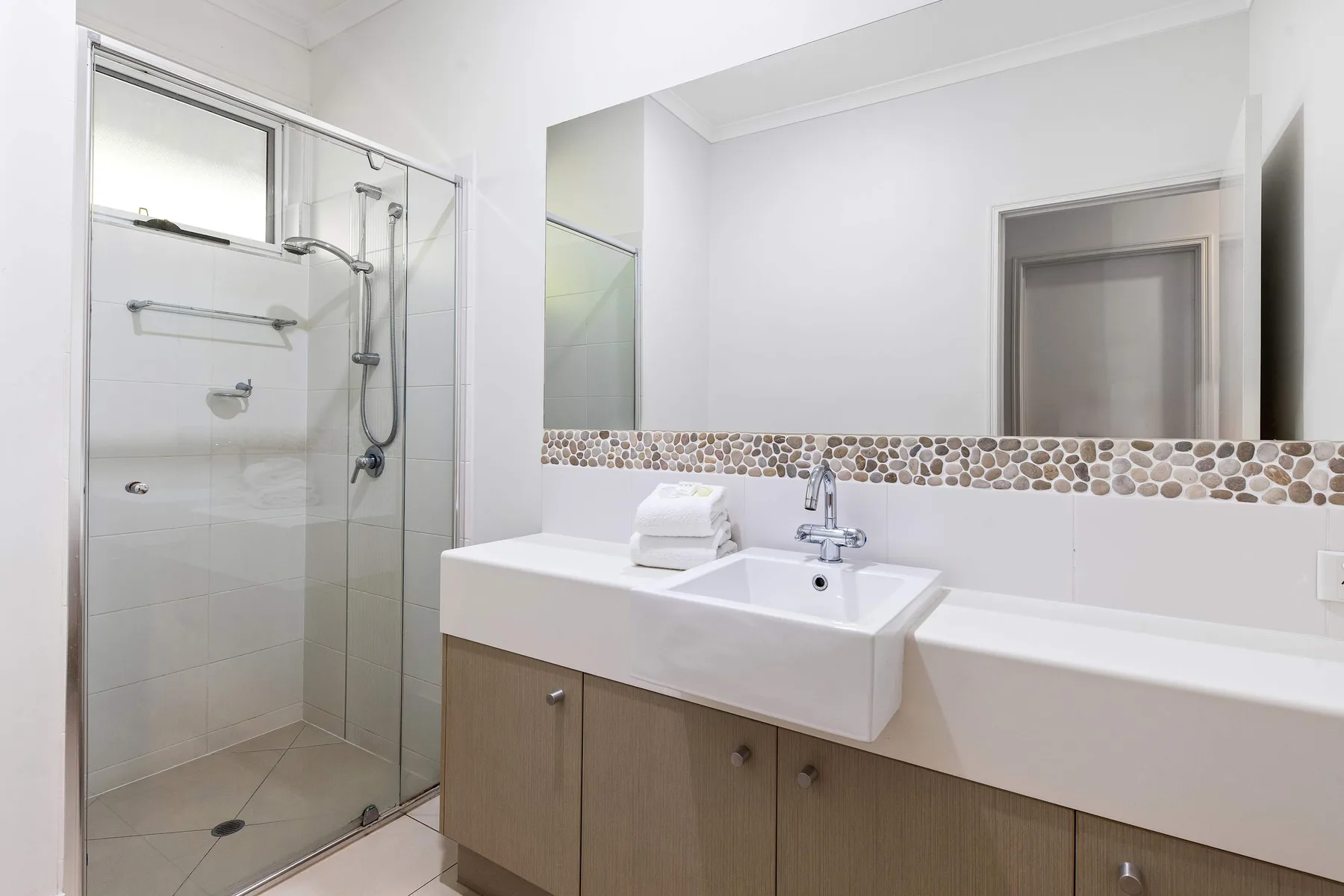 A bright bathroom with a glass shower and a wide vanity.