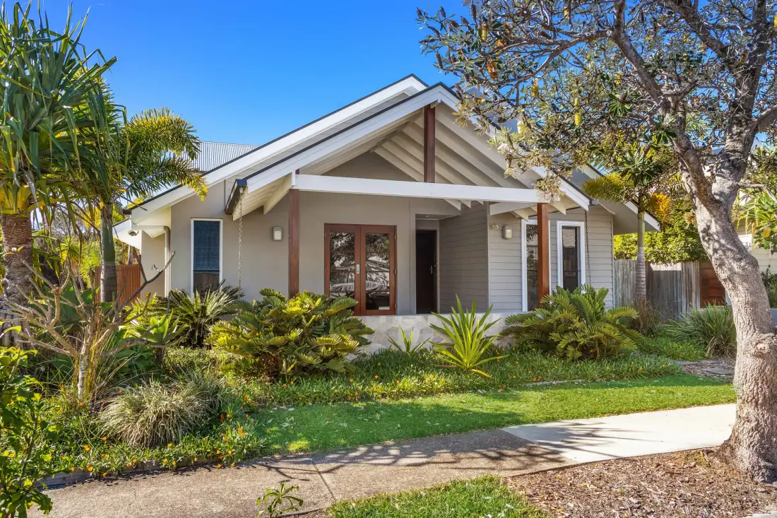 A single-story house with a front porch sits among trees and garden plants.