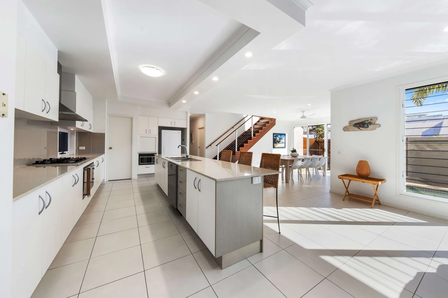 A bright open-plan kitchen and dining area with a central island and staircase.