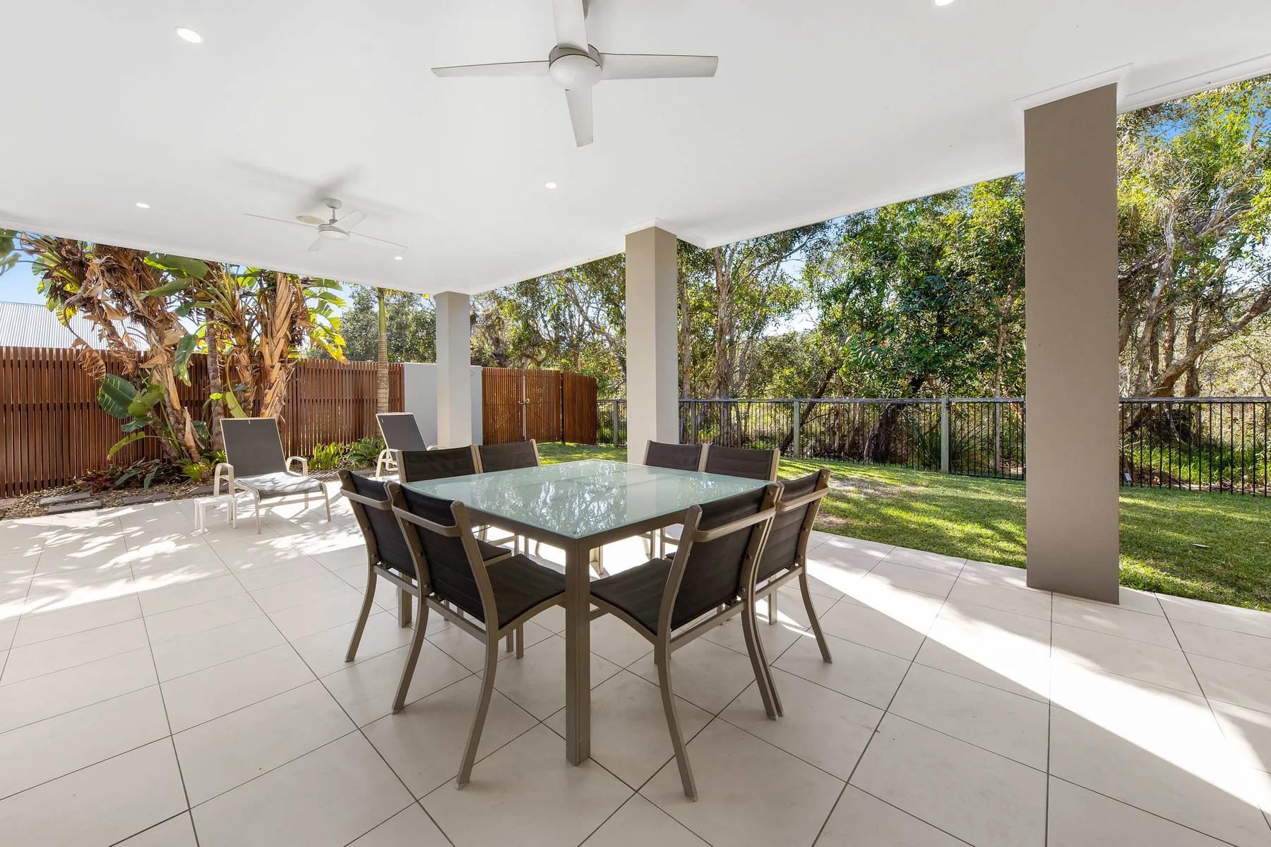 A covered patio with a glass-top dining table and chairs overlooks a green yard.