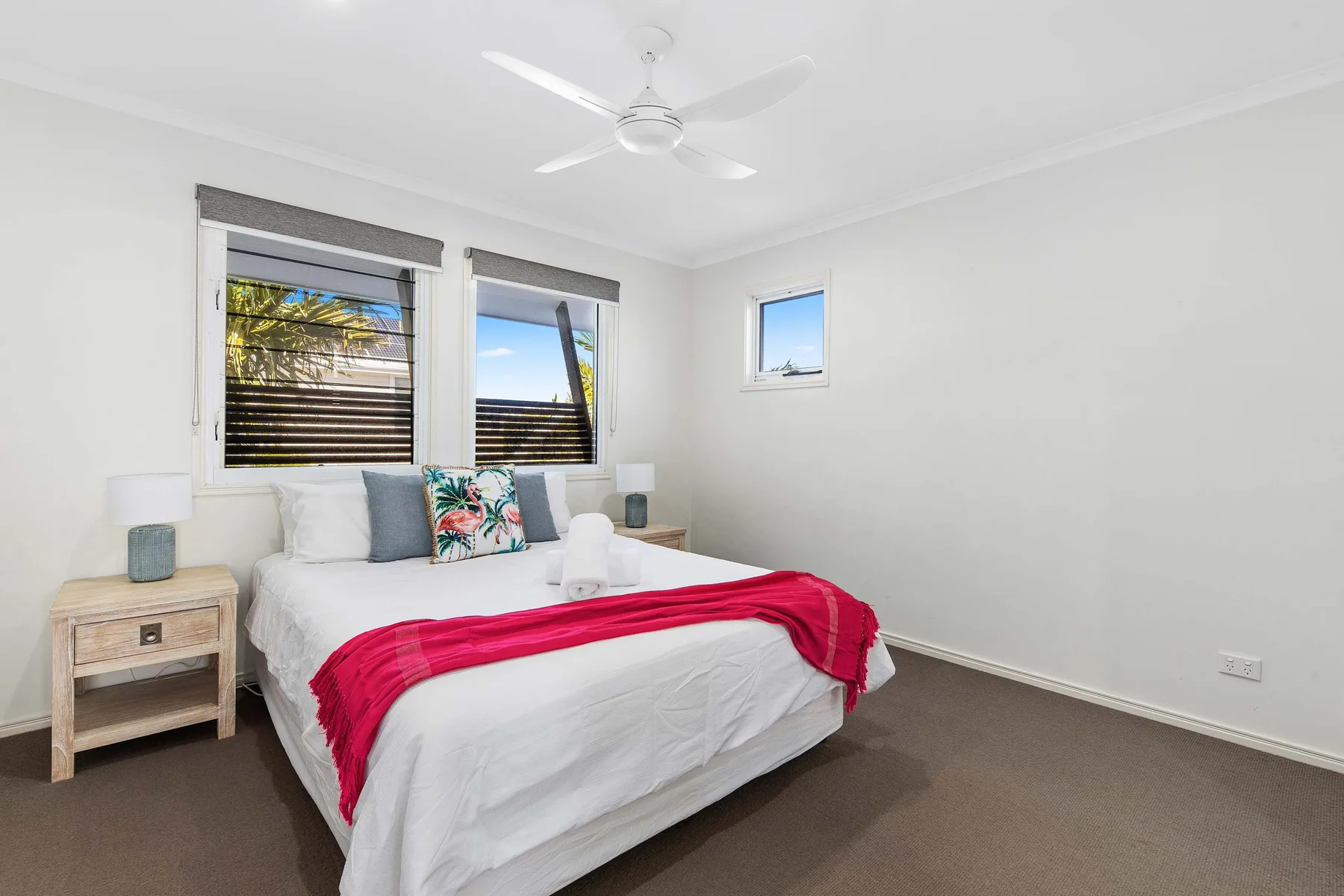 A bright bedroom with a neatly made bed and red throw.