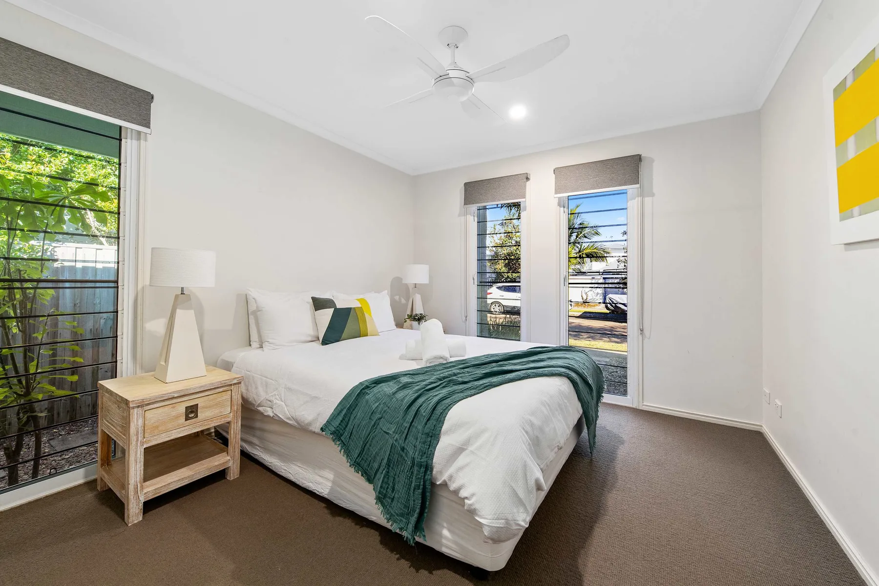 A bright bedroom with a bed and windows overlooking greenery.