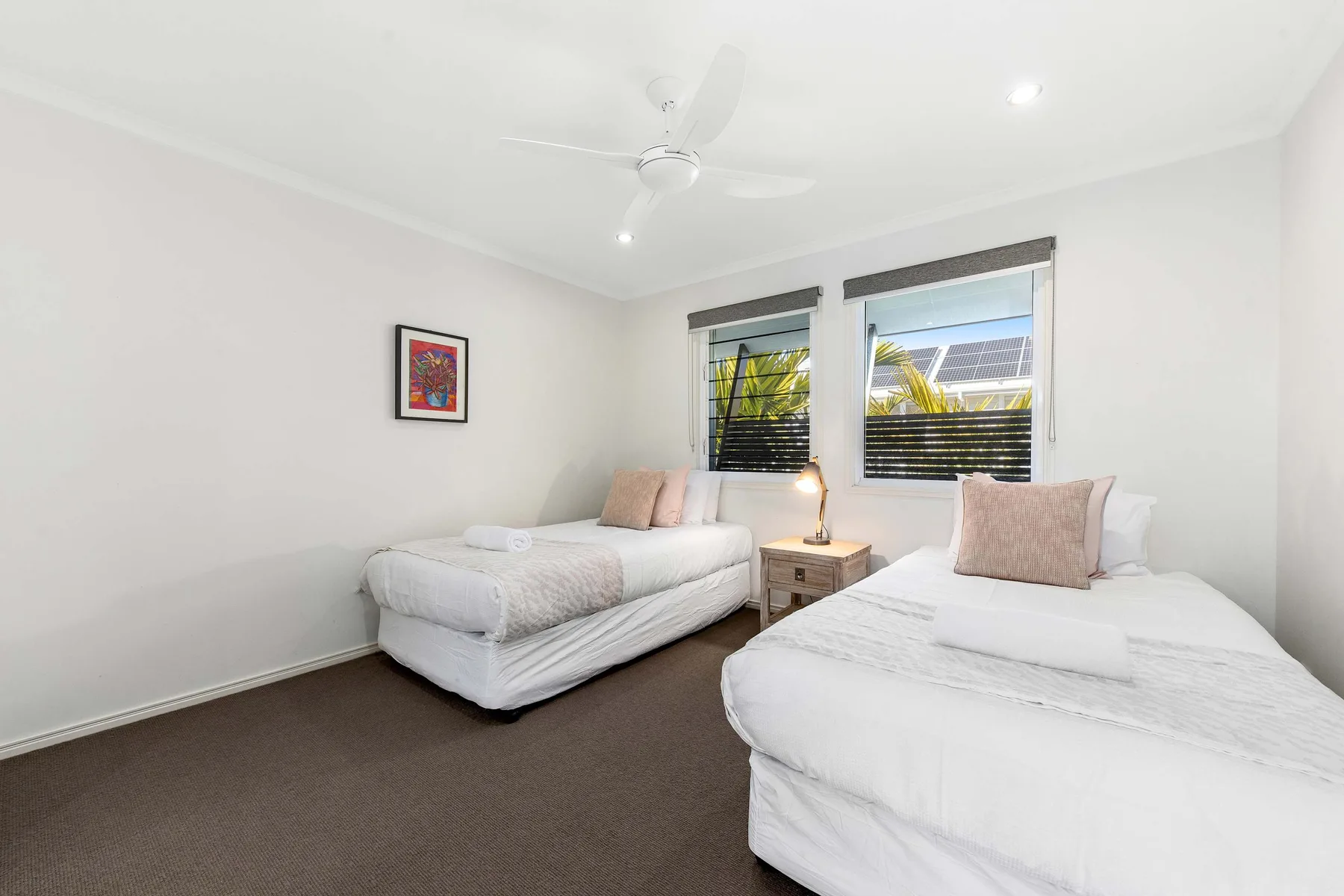 A bright bedroom with two beds and windows overlooking greenery.
