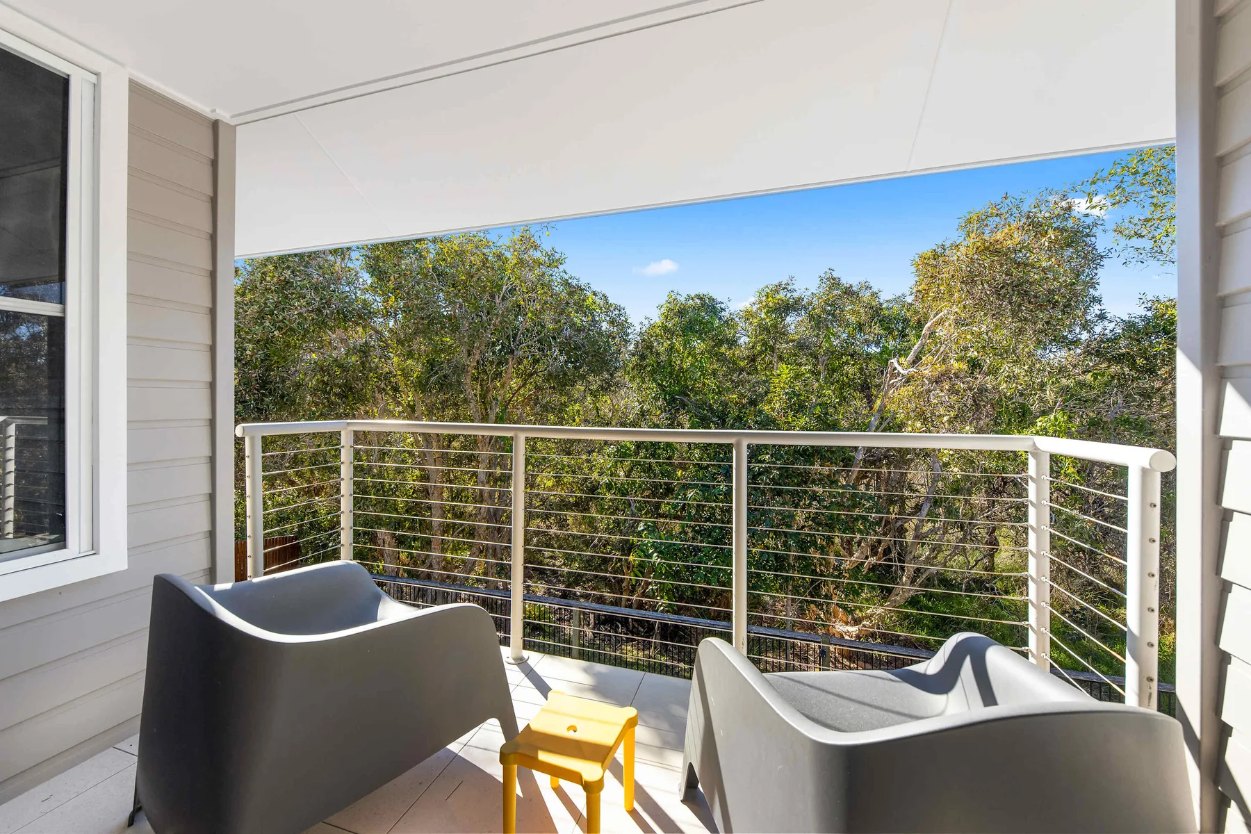 A covered balcony with seating overlooks leafy trees beneath a blue sky.