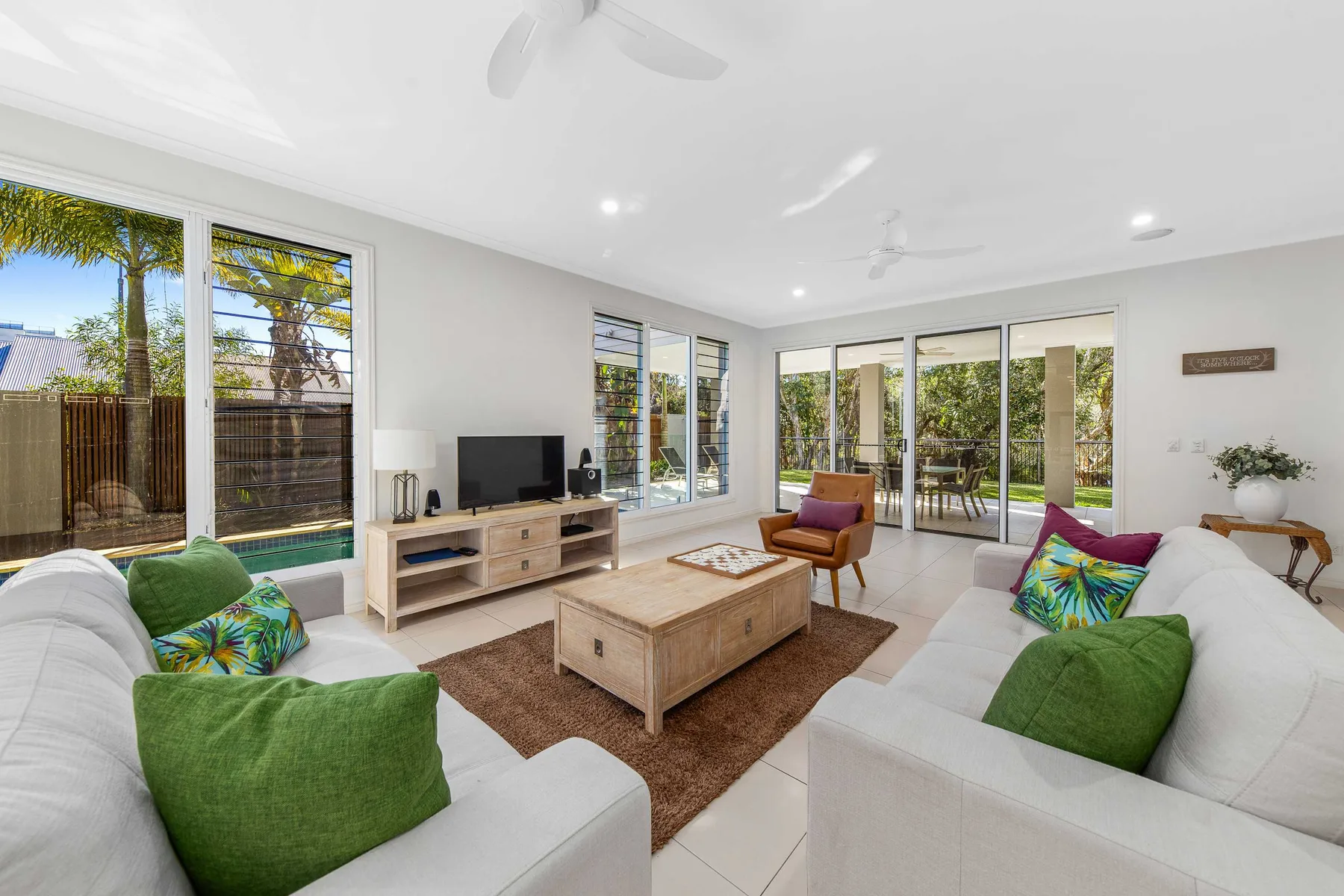 A bright living room with seating, a television, and large windows opening to a garden.