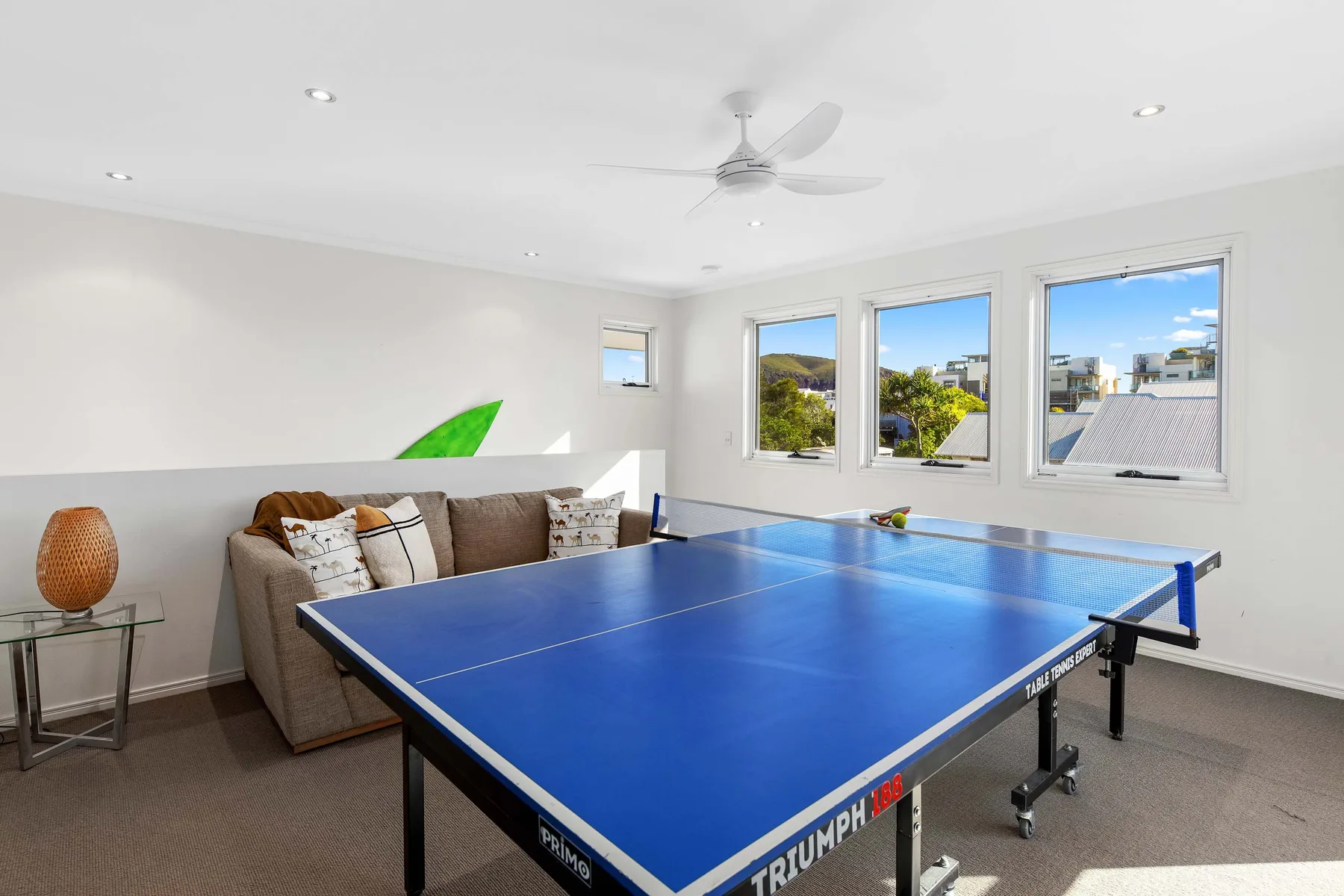 A bright recreation room features a blue table tennis table and seating.