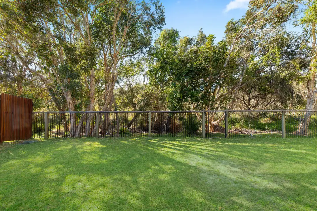 A grassy yard with a metal fence and leafy trees.