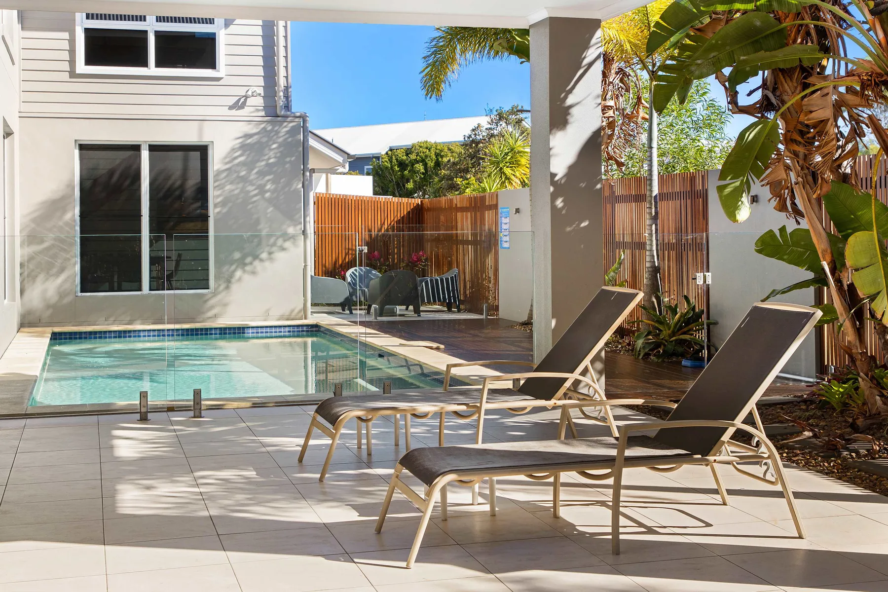 A tiled patio with a small pool and lounge seating beside the house.
