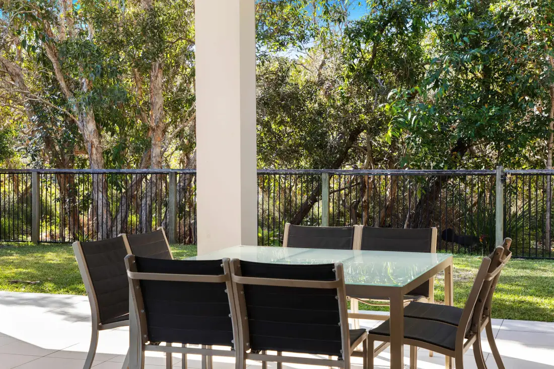 An outdoor dining area with a table and seating overlooks a leafy yard.