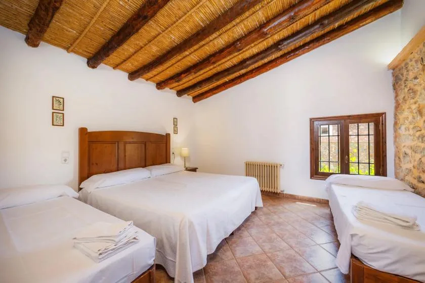 A bedroom with white-covered beds beneath exposed wooden ceiling beams.