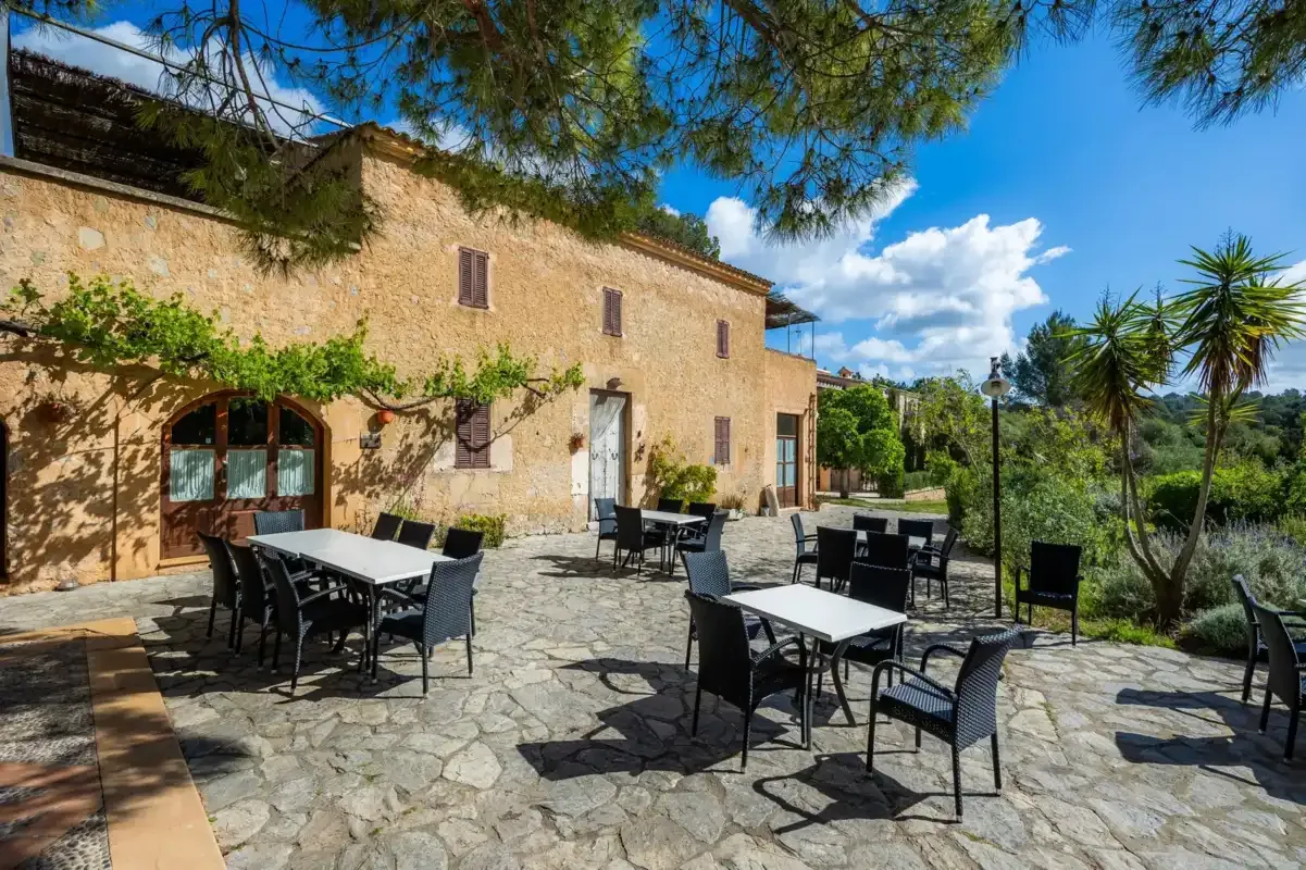 A stone-paved outdoor dining area with tables and chairs beside a rustic building.