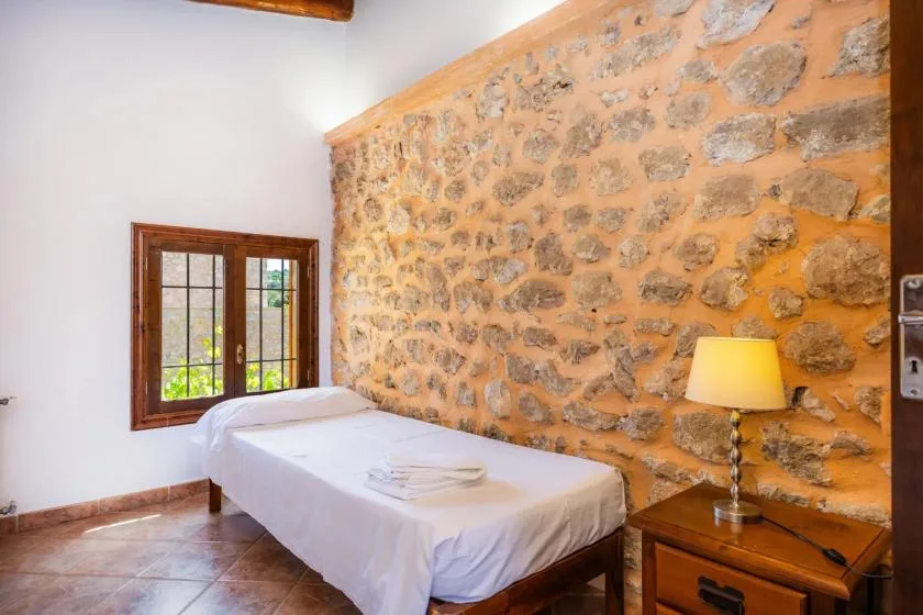 A bedroom with a single bed beside a stone accent wall and window.