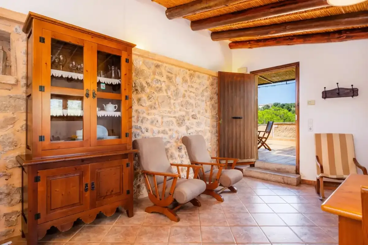 A rustic sitting room with wooden seating and a glass-fronted cabinet.