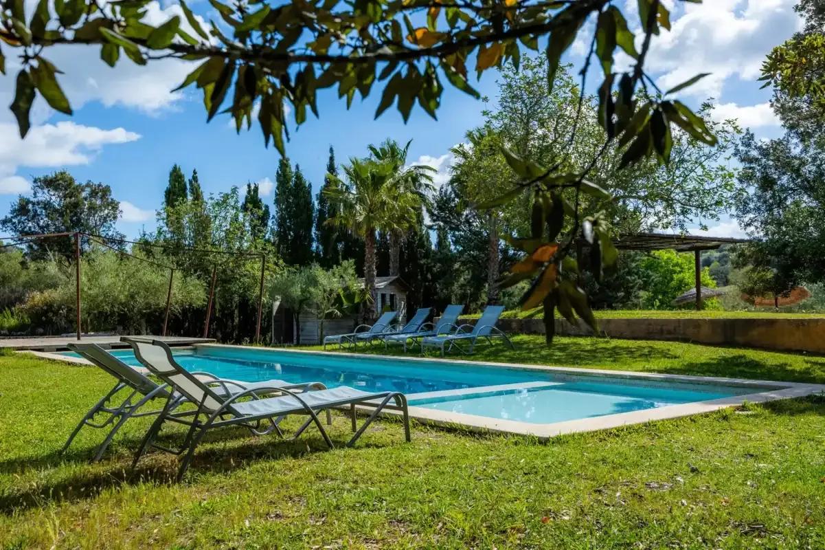 An outdoor swimming pool is surrounded by grass, trees, and reclining seating.