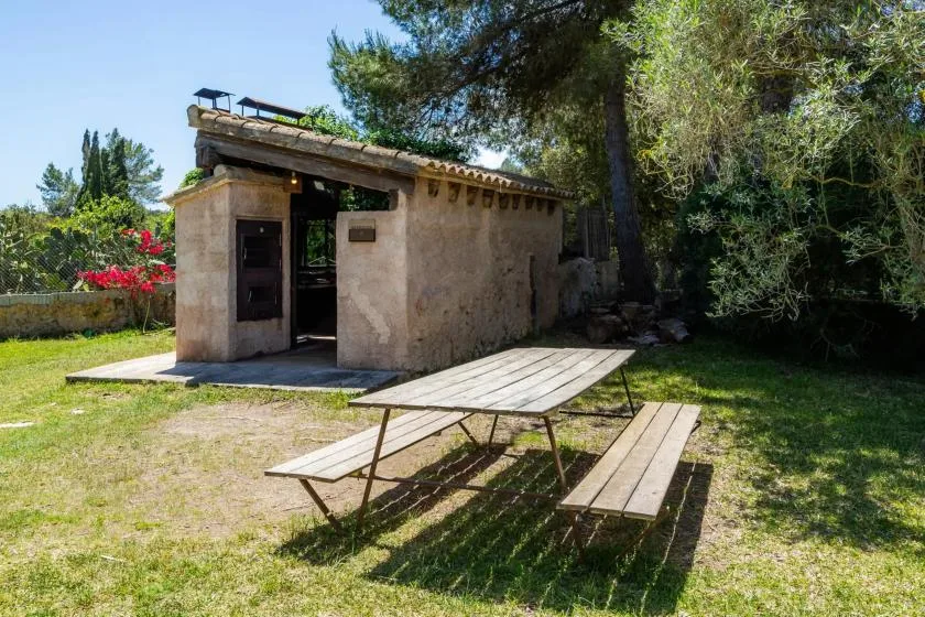 A small outdoor stone building stands beside a picnic table in a grassy yard.