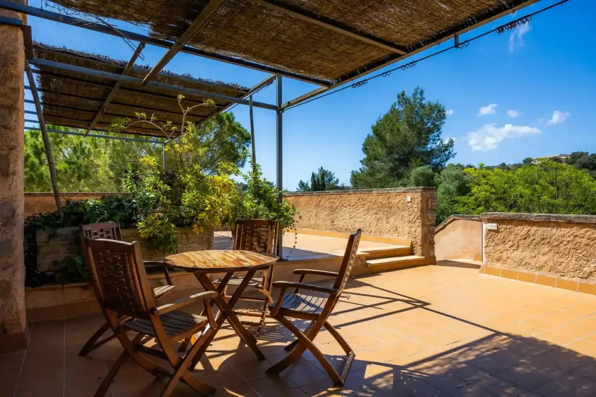 A sunlit outdoor terrace with wooden seating beneath a woven shade canopy.