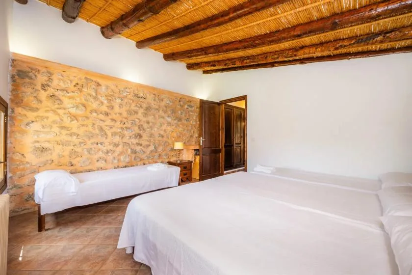 A bedroom with white beds, a stone wall, and exposed wooden ceiling beams.