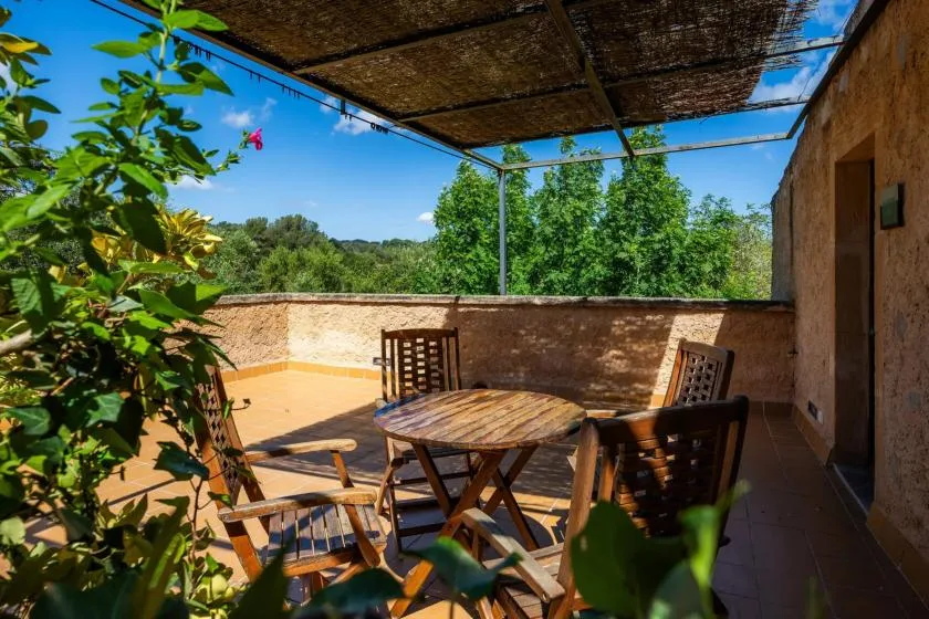 A shaded outdoor dining terrace with a wooden table and seating overlooks green trees.