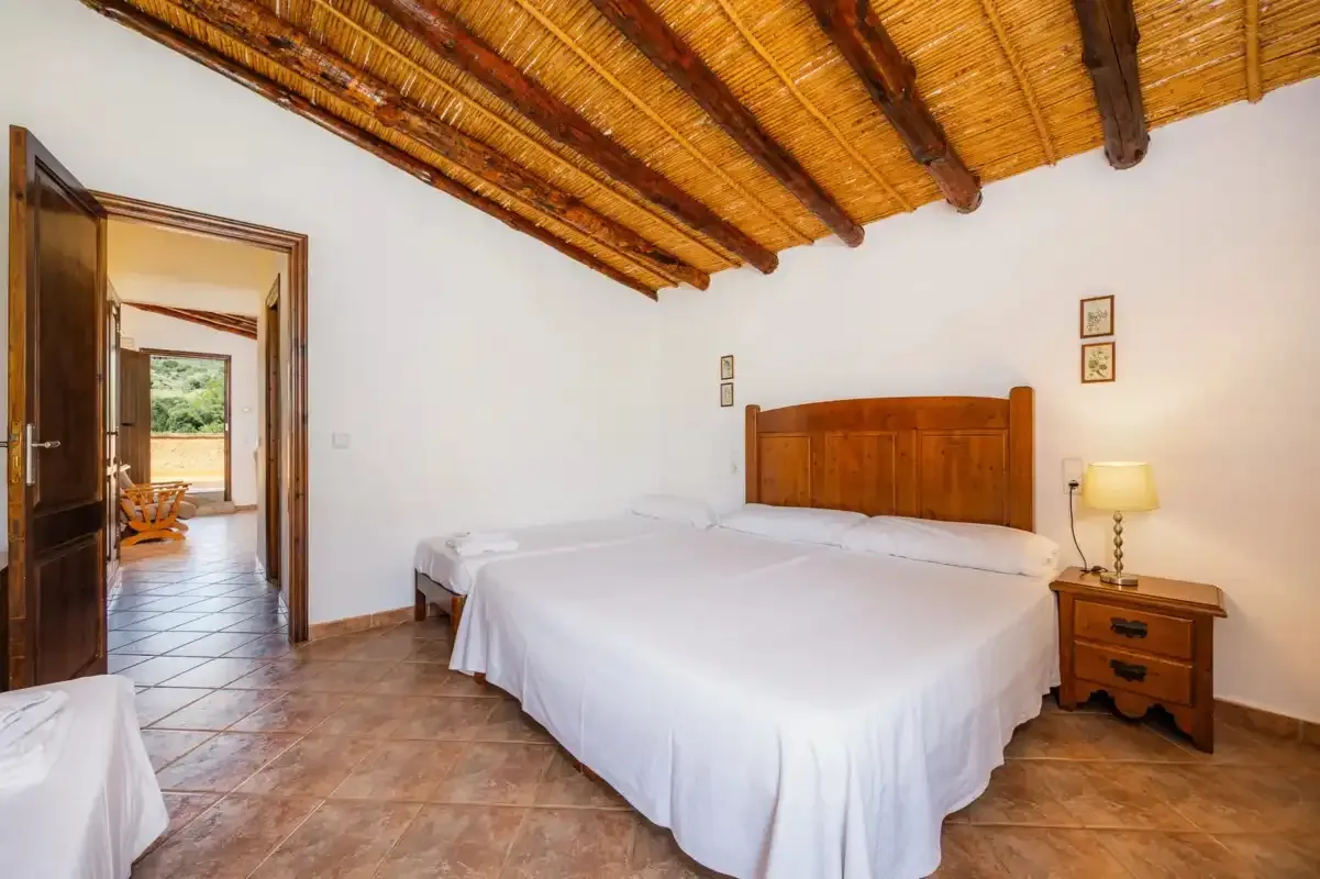 A bedroom with a large bed beneath a wooden-beamed ceiling.