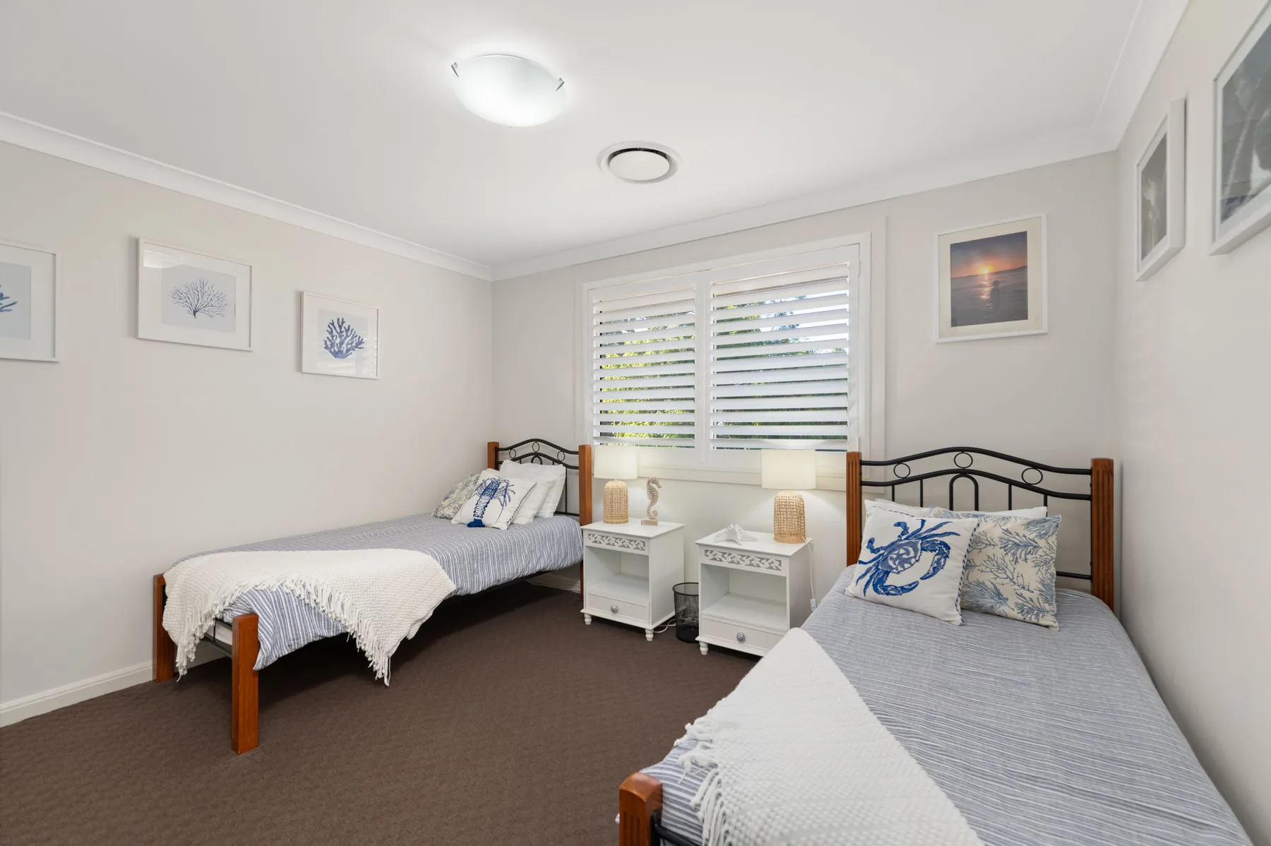 A bedroom with two beds and a window with white shutters.