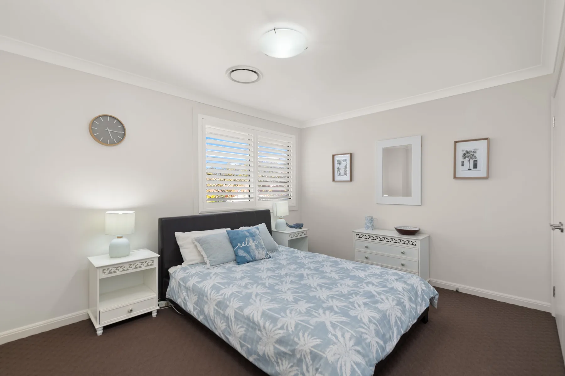 A bright bedroom with a bed beneath shuttered windows.