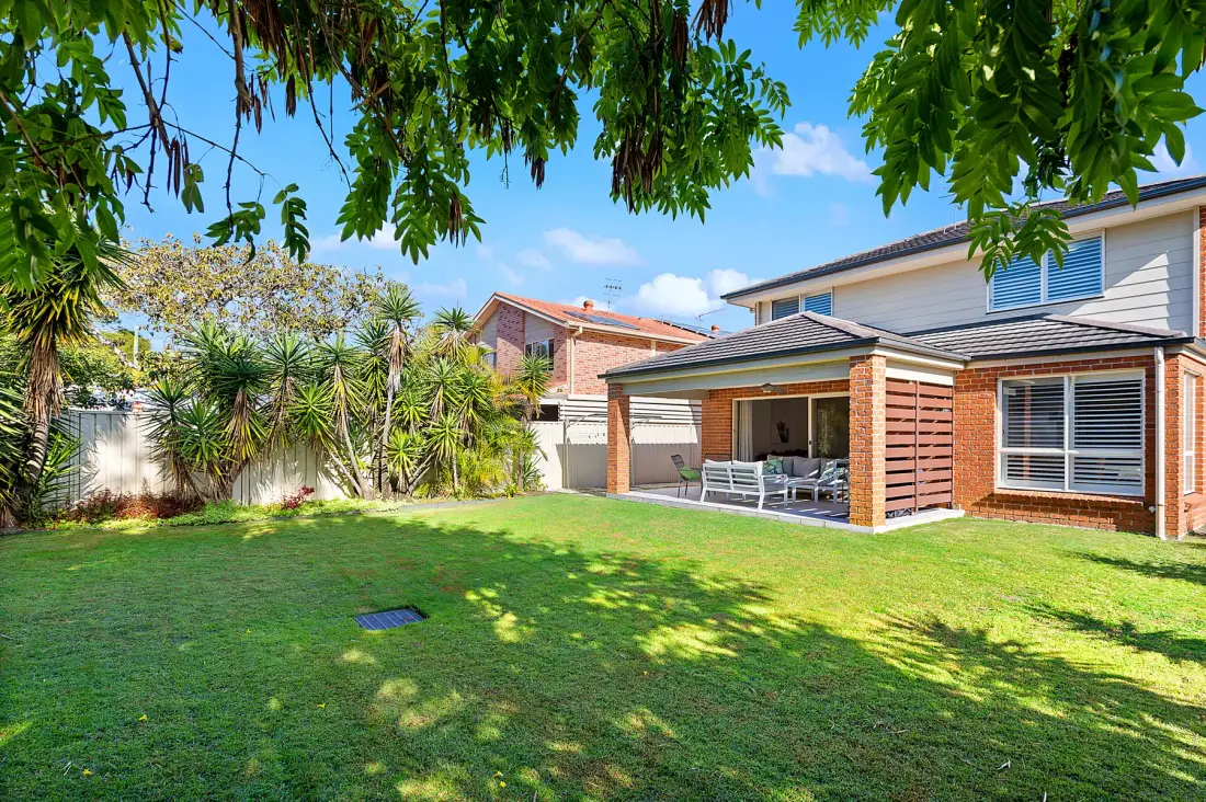 A landscaped backyard with a lawn, leafy trees, and a covered patio.