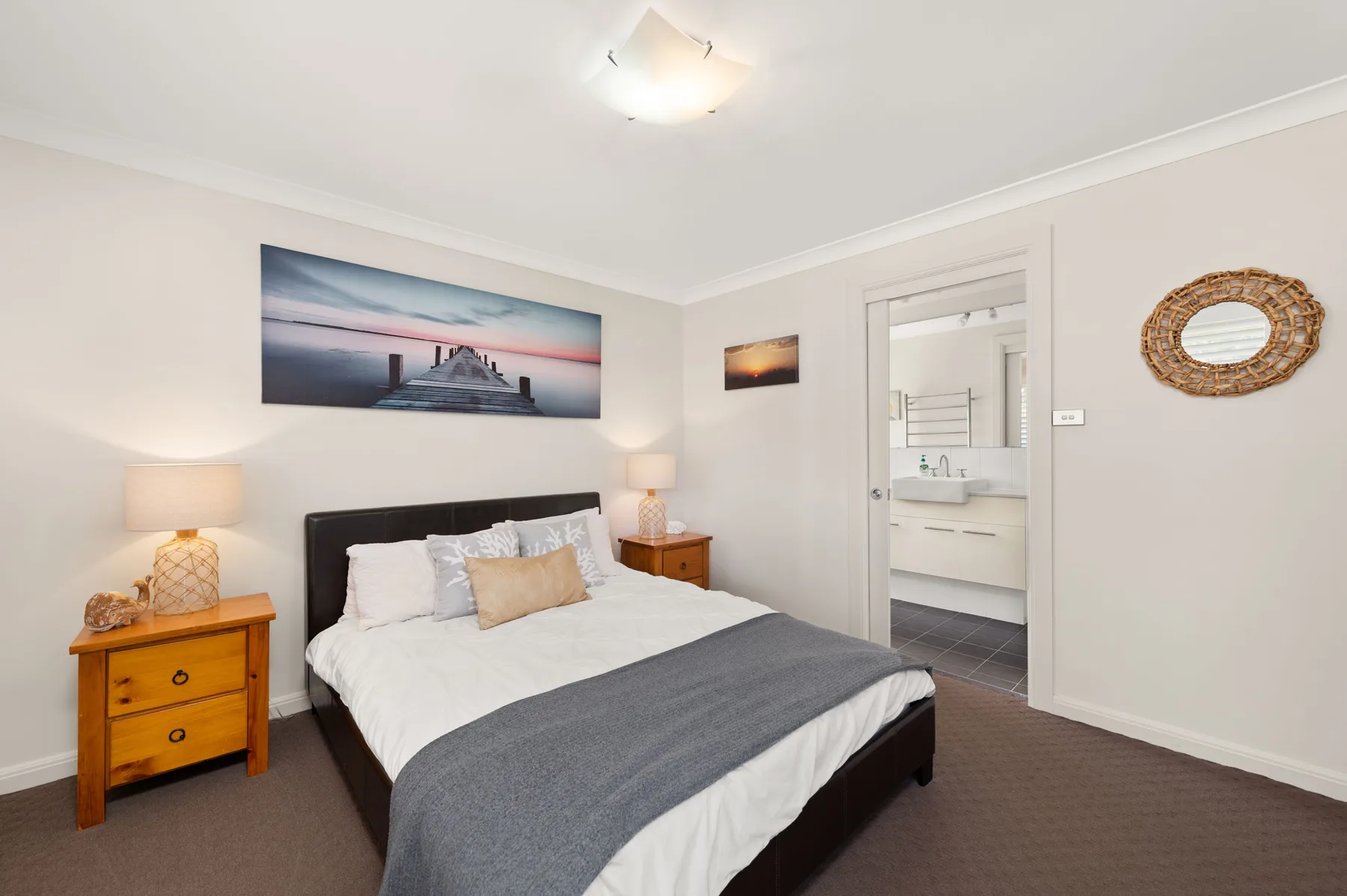 A bedroom with a neatly made bed, bedside tables, and coastal wall art.