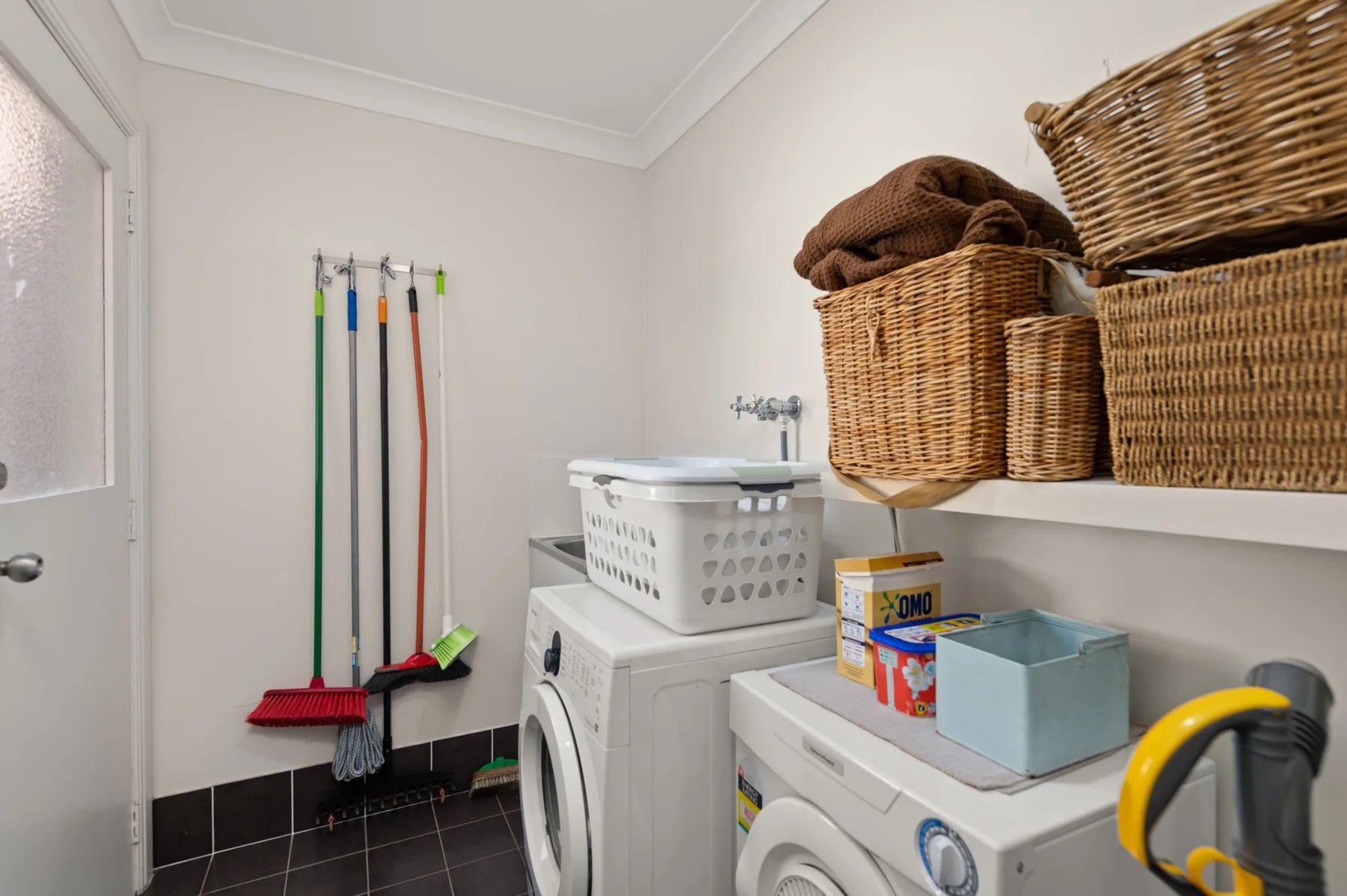 A laundry room with washing machines, storage baskets, and cleaning tools.