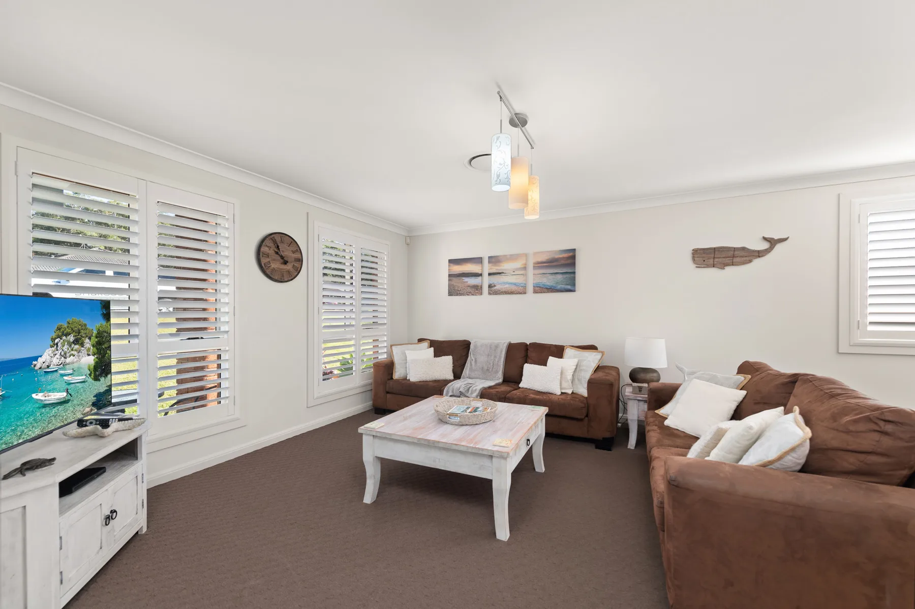 A bright living room with brown seating, a coffee table, and wide shuttered windows.