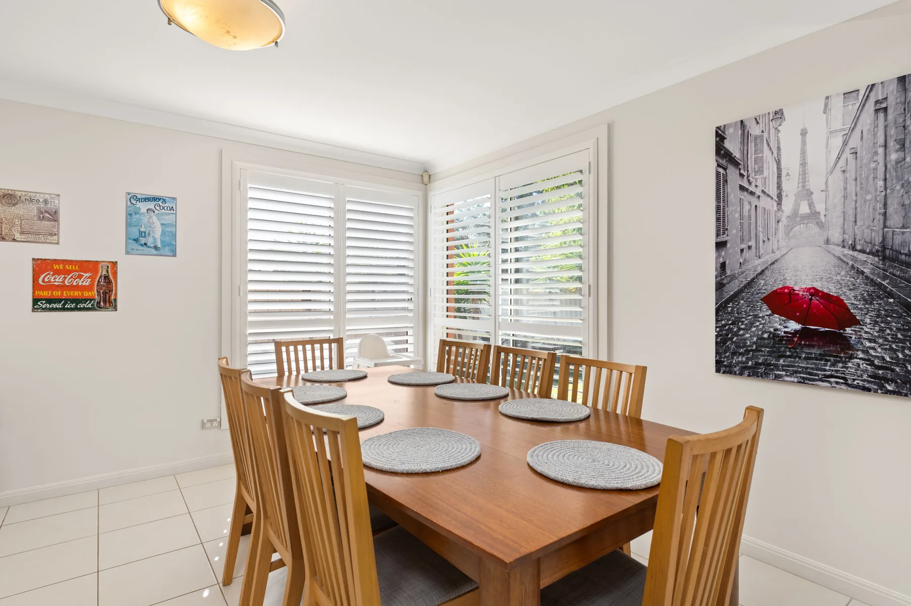 A dining area with a wooden table and chairs beside shuttered windows.