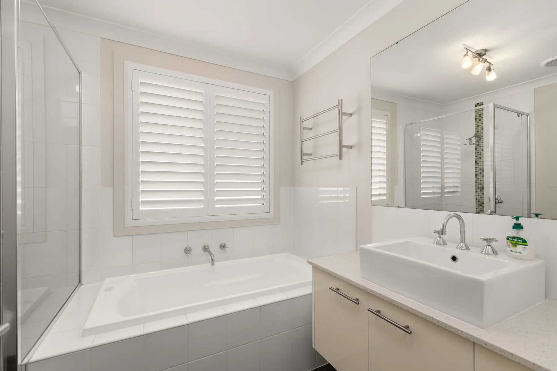 A bright bathroom with a bathtub, vanity, and large mirror.