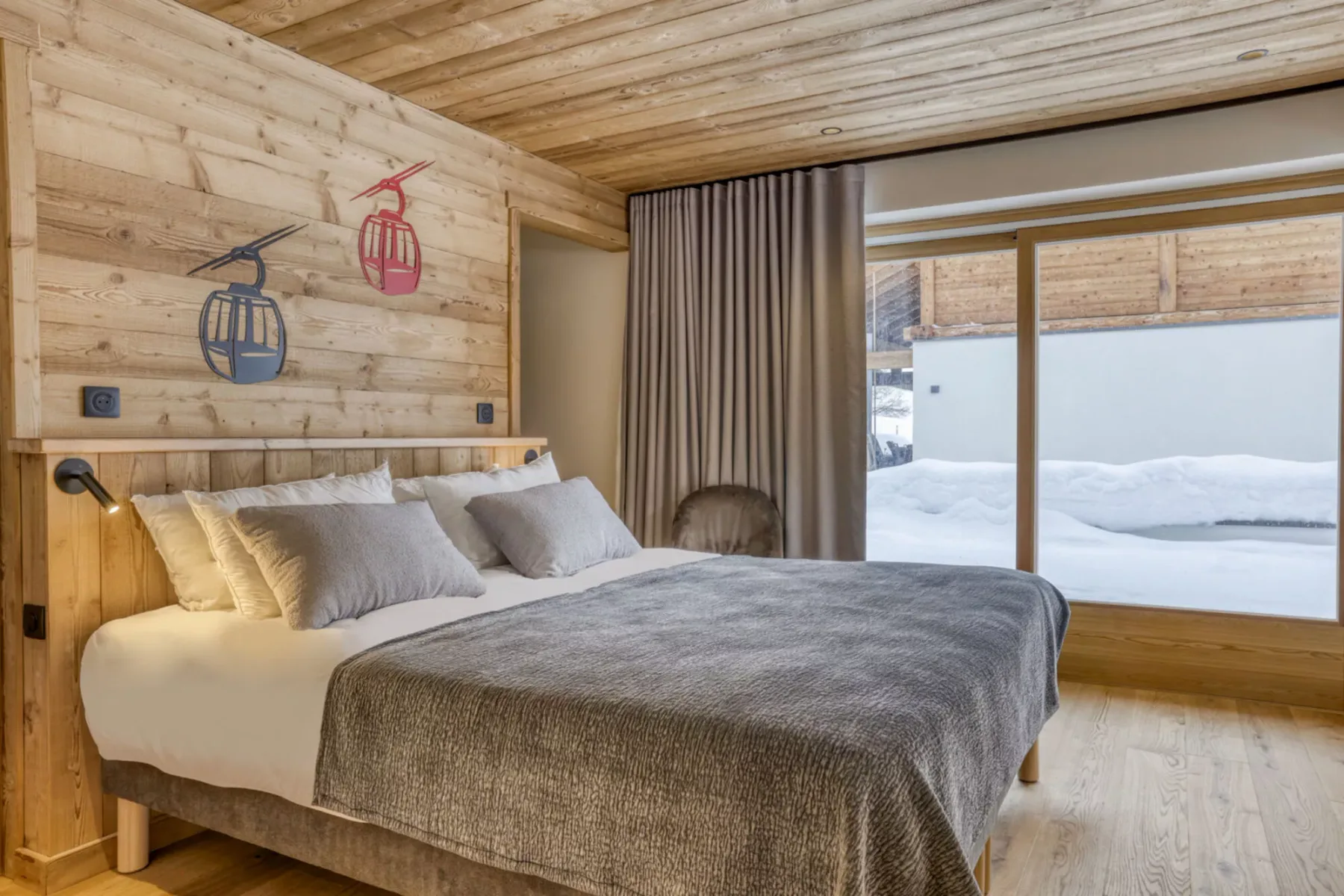 A bedroom with a bed beside a large window overlooking snow.