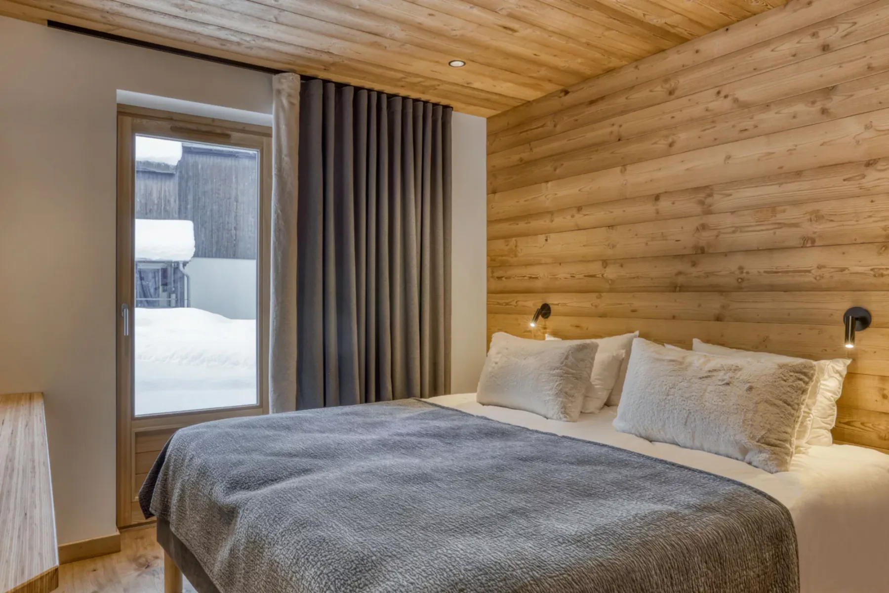 A bedroom with a bed dressed in gray bedding beside a window.