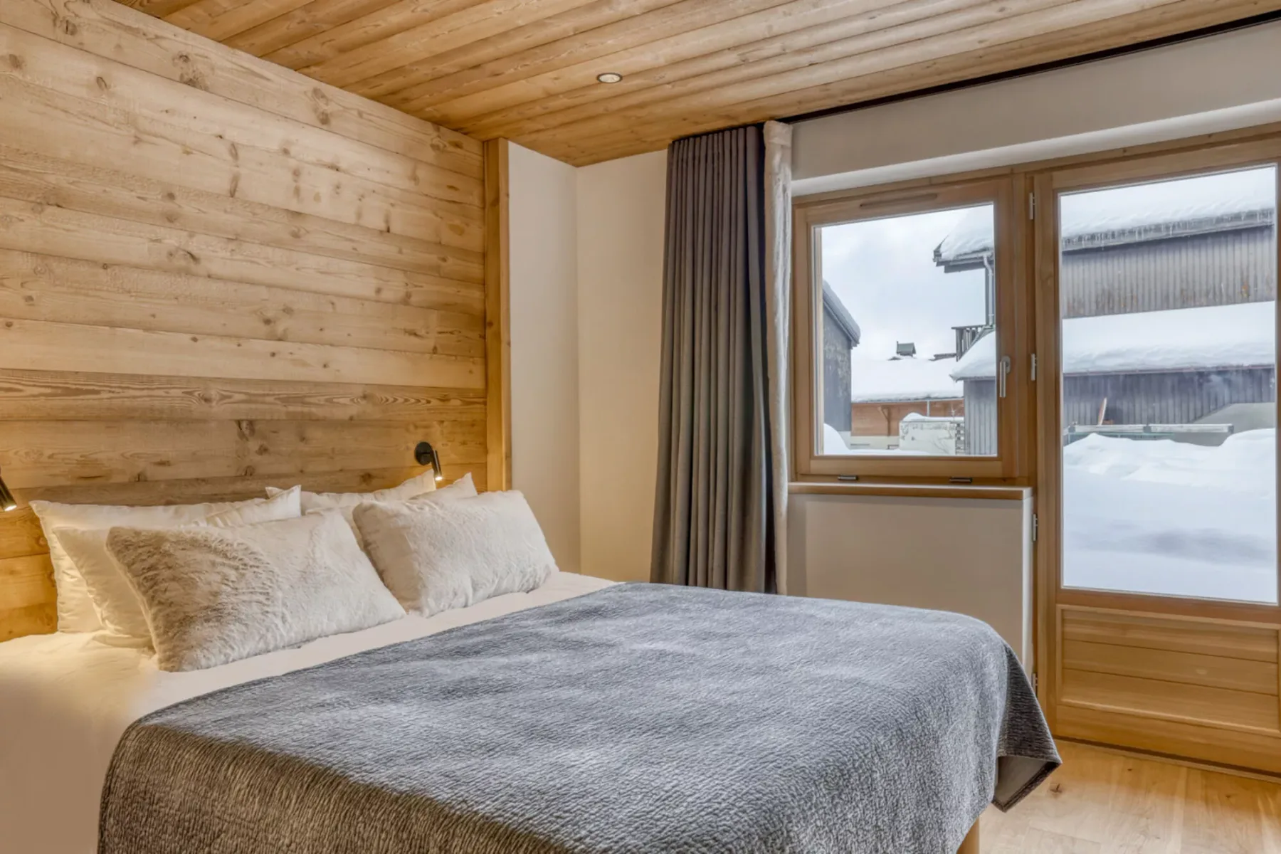 A bedroom with a bed beside large windows overlooking a snowy scene.