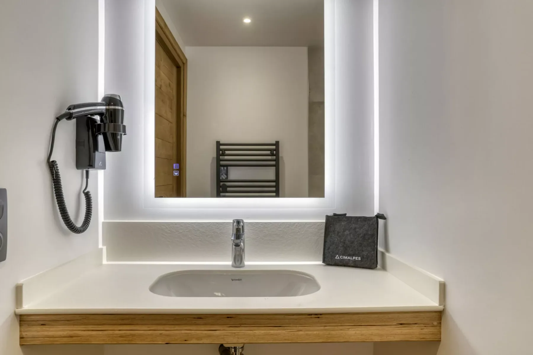 A bathroom vanity with a sink sits beneath a large illuminated mirror.