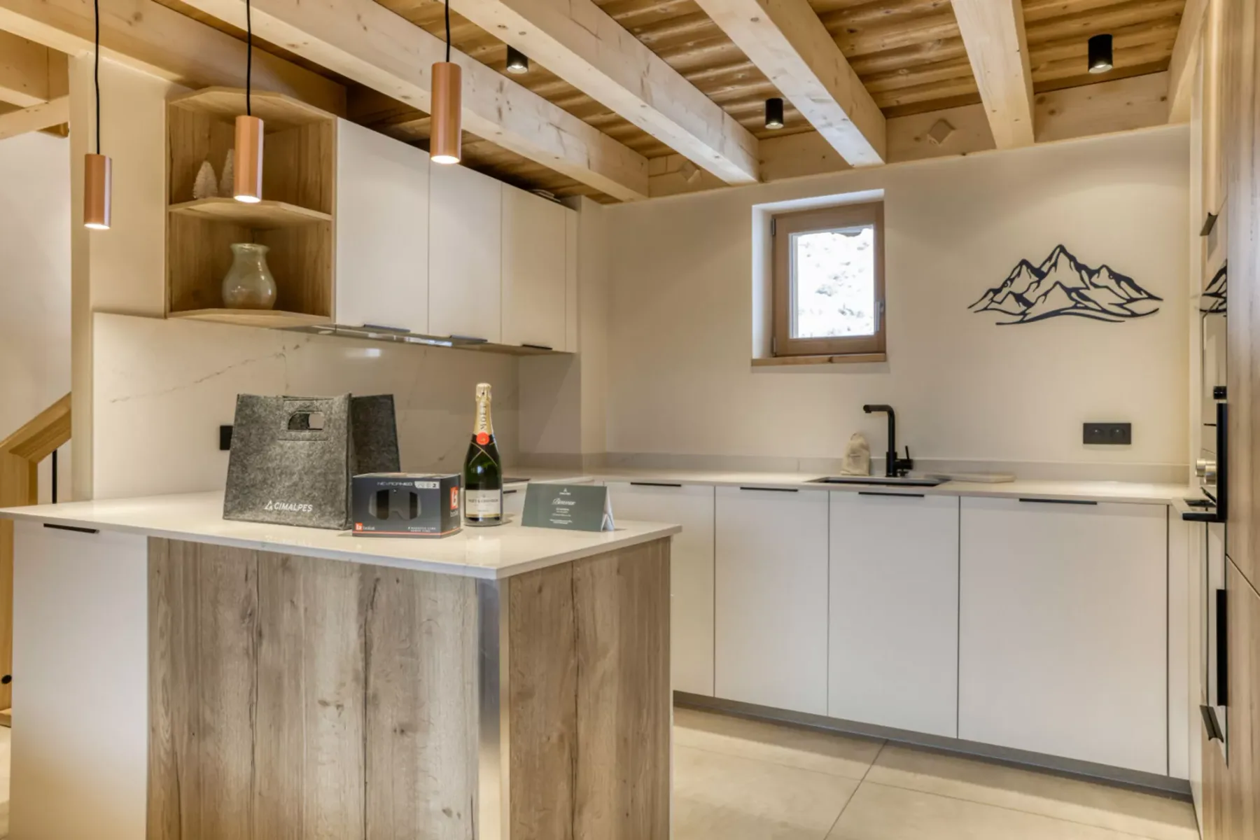 A bright kitchen with white cabinets, a central island, and exposed wooden ceiling beams.