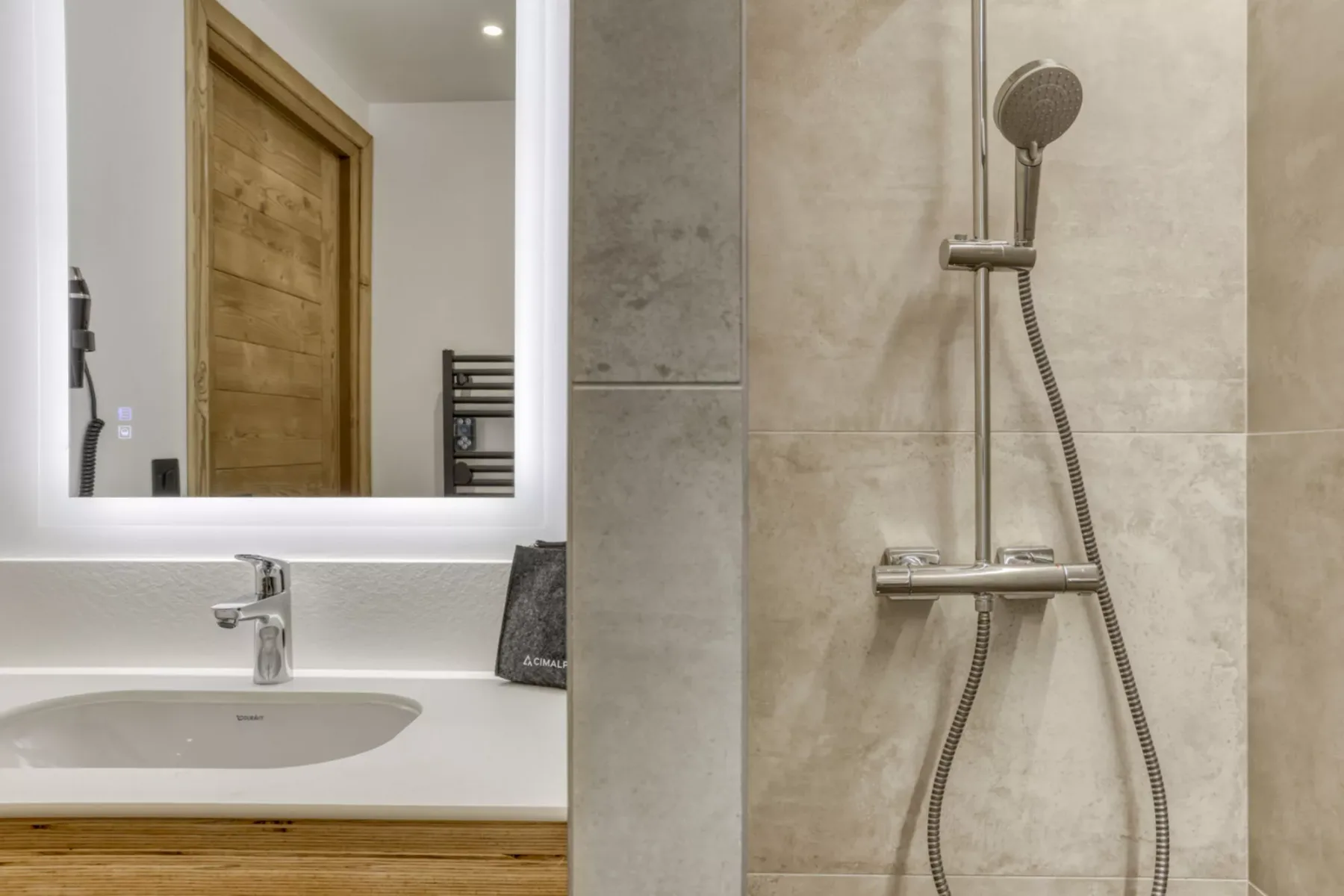 A bathroom vanity and mirror sit beside a tiled shower with a handheld showerhead.