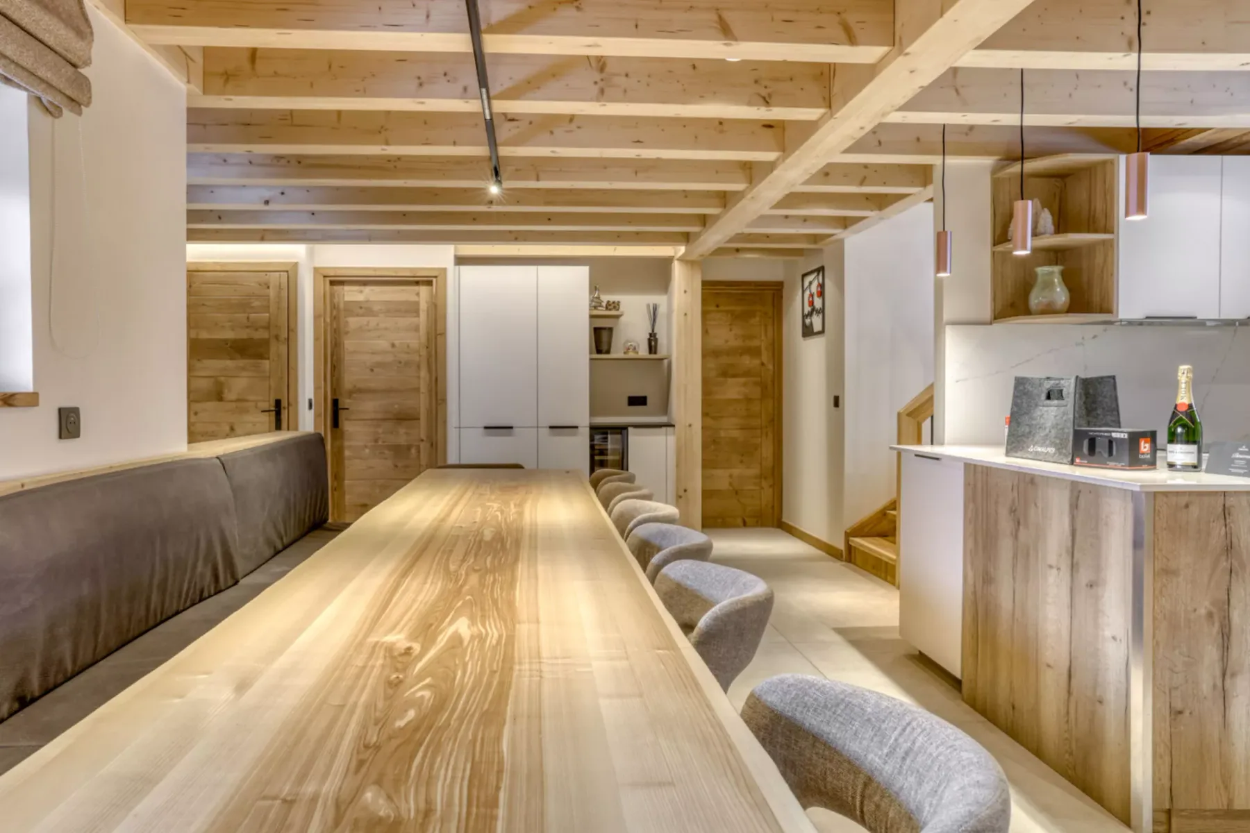 A dining area with a long wooden table and upholstered seating beneath exposed ceiling beams.
