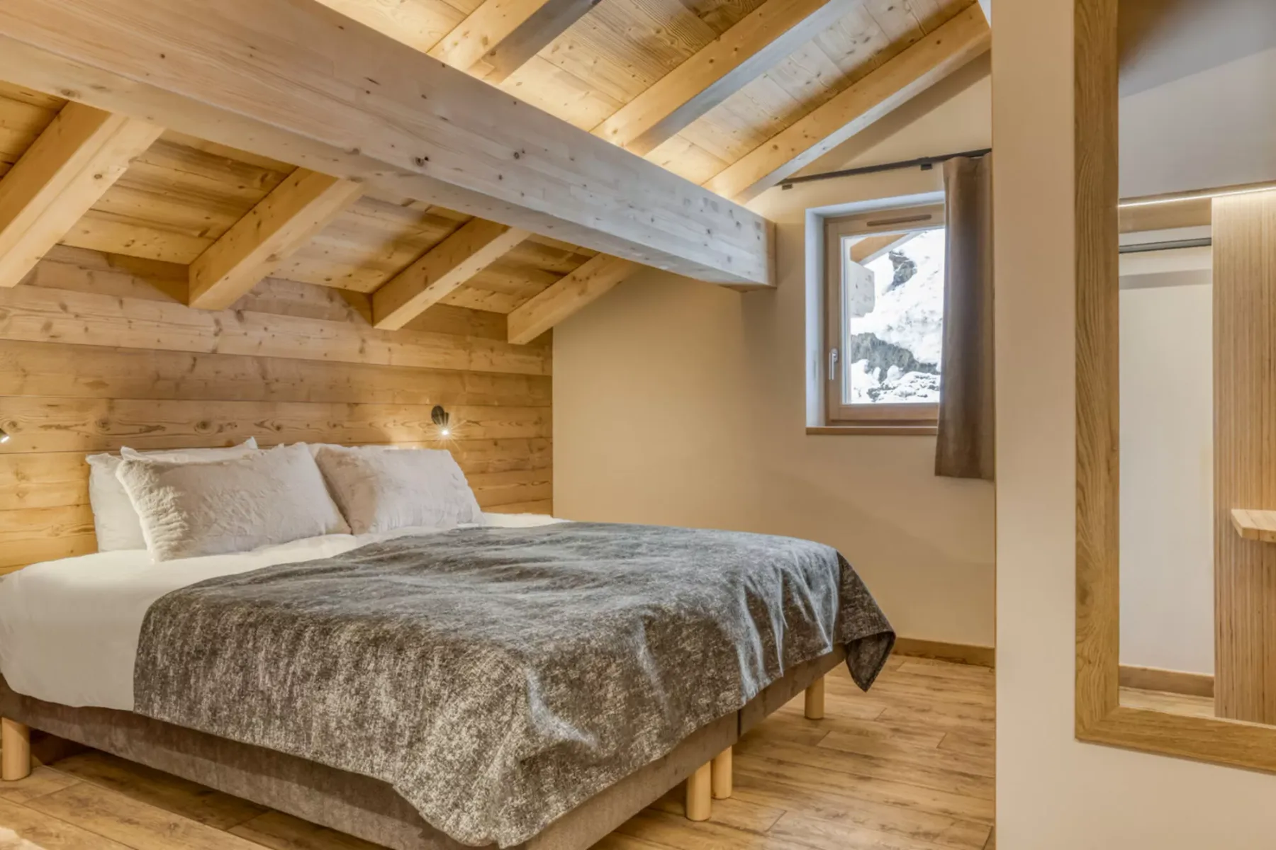 A bedroom with a bed beneath exposed wooden ceiling beams and a small window.