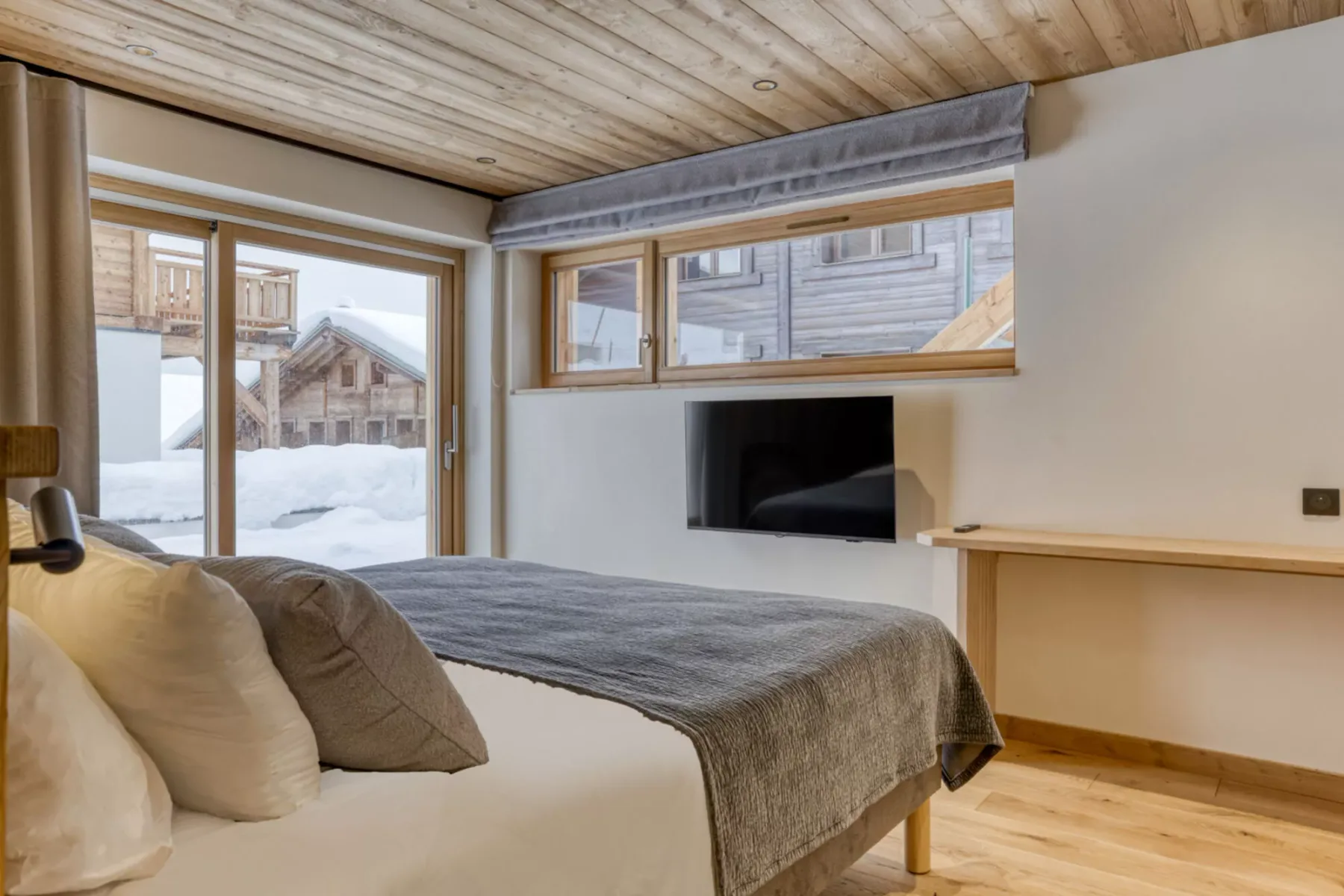 A bedroom with a bed beside large windows overlooking a snowy scene.