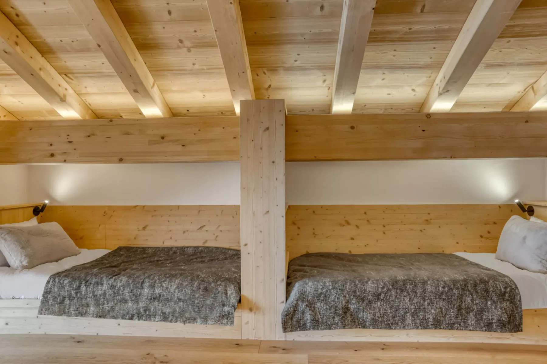 A wooden bedroom with two beds beneath a low timber ceiling.