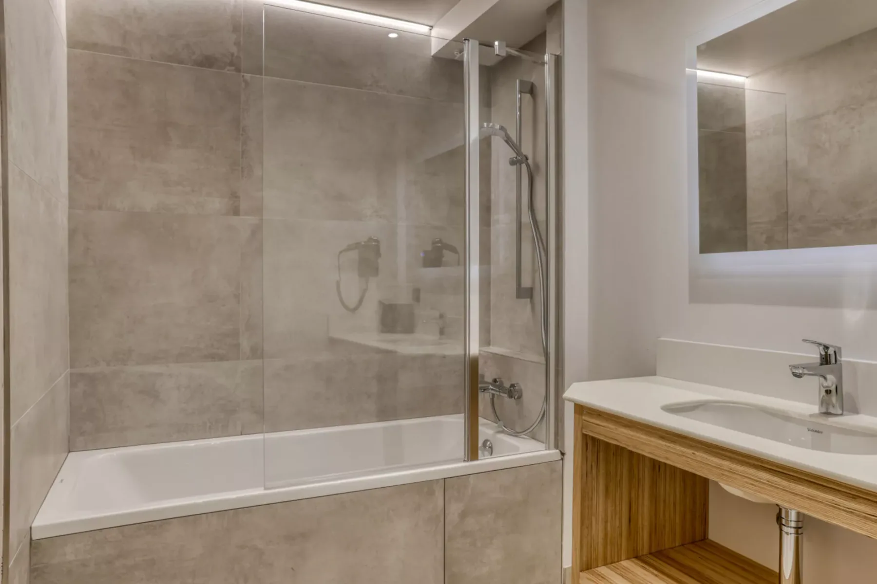 A modern bathroom with a glass shower screen and a wood vanity.